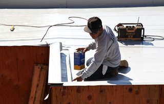 Dwell Home Venice: Part 14 - Photo 8 of 9 - A roof installer from J.T. Harris finishes installing the Versico PVC membrane on a garage roof parapet. The parapet will have a black metal coping installed as the final finish.