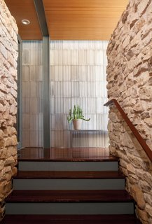 A striated concrete wall designed by Pollen Architecture & Design contrasts with the rough limestone rock of the home’s existing stair column.