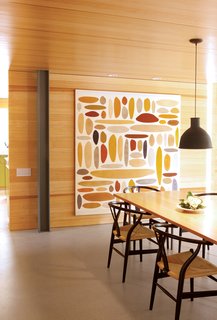 An abstract painting by Michael Young complements the glow of the dining room’s pine walls. A collapsible silicone lampshade by Swedish designers Form Us With Love for Muuto hangs above a Macek Furniture Company table.