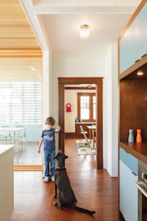 To help define the kitchen, the architects designed a wall of storage with cubbies on one side and a pantry with appliances on the other. Colorful doors add a playful touch, and DP3 Series cabinet pulls from Doug Mockett & Company keep the surfaces streamlined.