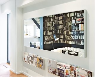 A Renovated Flat in Moshe Safdie's Habitat '67 - Photo 7 of 8 - The walls in the downstairs den are covered in Deborah Bowness’s Genuine Fake Books wallpaper and a set of String bookshelves. The leather chesterfield sofa is by Natuzzi.