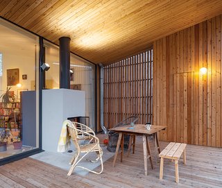 A collection of vintage furniture, including a rattan armchair and a drafting table, is gathered around the terrace fireplace, which shares a volume with the hearth in the adjacent living room behind. Outdoor sconces are from iGuzzini.