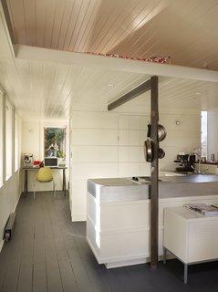 Tiny 1920s Garage Transformed Into a Charming Studio - Photo 6 of 8 - A utilitarian core contains the kitchen, bathroom, closet, and loft ladder. The kitchen’s walls are clad with recycled wooden boards trimmed with horizontal battens that hide the oven and refrigerator from view.