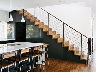 The Dora pendant lights in the kitchen are from Rejuvenation; quartz countertops are by Cambria and the custom bar stools are by Rocky Mountain Table Company. In Situ Studio designed the solid walnut steps with custom steel rails, a walnut hand rail, and a removable baby gate.