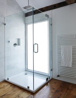 A glass-lined shower with a Hudson Reed shower head adds a modern touch to the second-floor bathroom in this farmhouse renovation. A pane of privacy glass lets natural light enter the room, illuminating the shower stall.