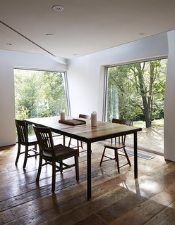 The new dining area is surrounded by swathes of glass. The windows were pivoted and installed at unusual angles in order to accommodate the undulating walls of the addition.