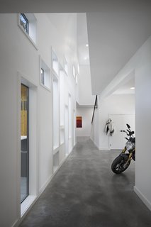 Beyond the staircase, at the heart of the main wing, a two-floor atrium rises from the concrete floor. Its array of windows, many of which are different sizes, connect the indoors with the central oak tree and the outdoors beyond it. The top of the wall slopes inwards, leaving the oak tree with room to grow.