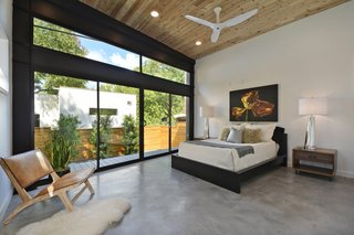 The master bedroom looks out at the garden through a full-height glass wall. The Ikea bed sits between Four Hands tables and lies beneath a floral photograph by Stacy Kirk. Opposite the bed, a Jaya chair is situated for quiet contemplation.