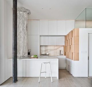 The careful coordination of color continues in the kitchen, where the gray and white marble backsplash, lit with faint orange lights, mediates between the ashen column and ochre cabinets.