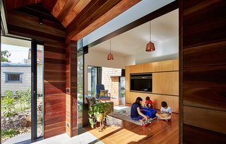 The owners furnished the living room with a mixture of new and old pieces, including a Hans Wegner lounger and Tuckbox coffee table. A timber-lined hallway leads out from it to the newer parts of the home. Sections of steel-framed double glazing separate and accentuate each "house" while letting in glimpses of sky.