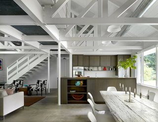 After: Completed in 2013, the roughly 1,500-square-foot cabin provides an open living area, now framed by white trusses and concrete floors. The dining table was acquired by the owner from a local inn, and is surrounded by the Eames molded plastic Eiffel side chairs from Design Within Reach. The kitchen features a Grohe faucet, a wood bowl from a shop in Harbert, and an IKEA vase.