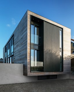 The house cantilevers slightly over a concrete wall, adding a touch of lightness and drama to its approach. Stairs beside to the cantilever lead to the entrance. On the upper level, a bedroom and family bathroom look out through the windows of the cantilevered façade.