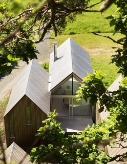 A rear deck is nestled behind the central cabin, flanked by the sleeping quarters. Inside, the dining table sits beneath a single hanging lamp.