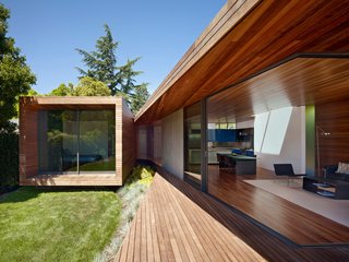 An Indoor-Outdoor Renovation for a 1950s Ranch House in the Bay Area - Photo 1 of 8 - The larger volume of the addition, consisting of kitchen, living, and dining spaces, loops around to the smaller bedroom through a wooden passage. The same ipe, with differing finishes, is used for both the interior and exterior. Expansive sliding glass doors by Fleetwood dramatically open up the living space to the outdoors.