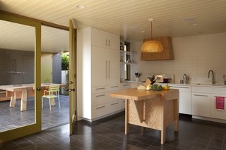 The kitchen island was also a custom design by Clementi and Smith-Clementi. The pendant light overhead is a BÖJA from Ikea reconfigured by the architects. The floor tiles are made of concrete and are from Granada Tile.