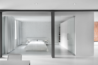 The bedroom is enclosed with a glass wall. A blackout curtain can be drawn closed for privacy. An IKEA cabinet and white lacquered shelves help to provide plenty of closet space.