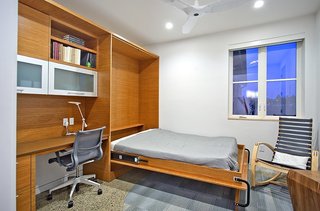 Here, a cabinet runs along the entire back wall of the den, incorporating a Murphy bed with desk, task lighting, and even ample storage space for belongings. By pulling down the Murphy bed, the den becomes a guest room.