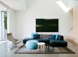 White walls and concrete floors define the ground level, where a Bend sectional and Metropolitan chair by B&B Italia, an Arper pouf, Bella coffee tables by HAY, and a Peace Industry rug furnish the main living area.
