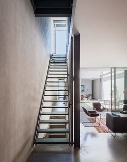 Long, unobstructed corridors along the spine of the house provide ample cross-ventilation during warmer months—as well as sightlines that unite different areas of the home’s narrow, linear footprint. "When you’re in the back of the building, you can literally see the front door of the person across the street," says architect and resident Philippe Baumann. Thick industrial glass lines the footing of the stairwell with subtle transparency, allowing light to also traverse the space vertically.