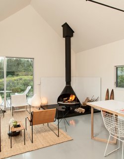 A Cluster of Cabins in a Former Quarry Makes a Simple Vacation Escape - Photo 3 of 13 - Among the three pavilions are the standard comforts of any home: A kitchen, living space, and dining area are situated in an open floor plan in the main cabin, where a collection of vintage pieces—including leather lounge chairs from Belgium and a Preway fireplace—mix with white Bertoia wire chairs and Noguchi table lamps.