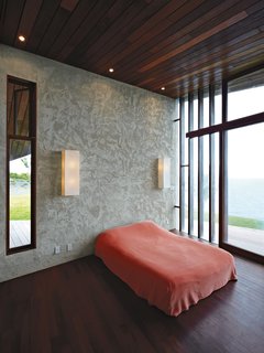 In the master bedroom, a basic platform bed and Ikea wall lights keep the attention on the ocean views afforded by the floor-to-ceiling windows.