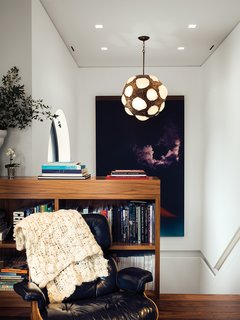 At the top of the stairwell, a sitting area is outfitted with a vintage Eames lounge, a large Jack Goldstein painting, and a 1970s light fixture found by Marcovitz in Paris.