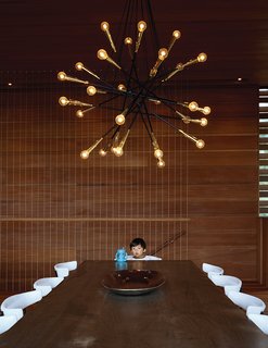 Wire stair balustrades create an airy vibe while reinforcing the linear wood detailing throughout. In the dining area, a Sputnik-style chandelier by Rewire in Los Angeles hangs above an oxidized maple table from BDDW and Clifford Pascoe chairs from Metropolis Modern.