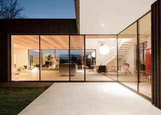 The entrance has a simple white ceiling, the dining table sits in a double-height space, and the living room has a warm spruce ceiling, subtly dividing the open floor plan. The interior flooring (a custom mixed shade of Invedra concrete) was also used on the patios, which help facilitate the indoor-outdoor cohesion.