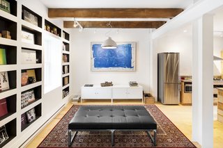 In the living room, and throughout the home, recessed "book nooks" are used to provide space-saving storage. The only seating in the room is a sleek black faux leather and steel daybed, fabricated by Montreal-based Surface Jalouse. Walls were removed to cohesively unite the living space and kitchen.