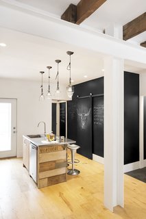 The couple's kitchen is an exercise in both sustainability and creativity. The island is wrapped with reclaimed scrap wood uncovered from the house during demolition. Chalkboard walls provide a whimsical canvas for graphic images and notes.