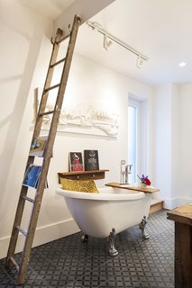 A new clawfoot tub sits next to an old wooden ladder that serves as a towel and magazine rack.