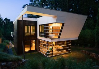 The house features a concrete rainscreen painted gray and Cor-Ten steel paneling around the exterior of the bedrooms. The horizontal louver theme around the dining room windows mimics the vocabulary established on the street-facing facade.
