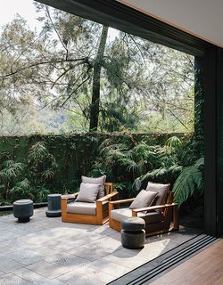 A Lush Retreat With a Sheltered Rooftop Pool in Mexico City - Photo 1 of 14 - Recinto lava stone lines a patio adjacent to the living room in designer Ezequiel Farca’s house in Mexico City. He designed the teak outdoor furniture, including two arm-chairs.