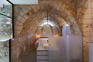 The master suite is housed in a cozy ground floor nook that takes advantage of the home’s original archways. Transparent and semi-transparent glass are used to create privacy without sacrificing scarce light. Understated sunken floor lighting adds a subtle accent to the perimeter.