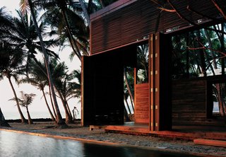 6 Modern Homes on the Water - Photo 1 of 6 - It’s hard to believe that this idyllic house sited in a coastal coconut grove in Nandgaon, India, is a mere hour’s drive from bustling Mumbai. For architect Bijoy Jain, principal at Studio Mumbai Architects, making the most of the muggy locale meant foregoing walls for louvers and slatted sliding doors—and opting for local materials to construct the airy home. "Response to weathering is critical along the seaside," he explains. The East Indian laurel, Burma teak, and palmyra woods will endure the seaside climate with an oiling after each monsoon. The pool that runs between the two structures of the home contrasts the choppy white-capped ocean with tranquil charm, making it a favorite spot for the vacationing family of four, who spend weekends here at the retreat.