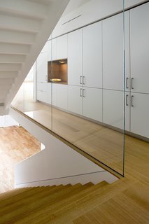 A custom staircase with wood risers is encased by glass panels. A wall of Henrybuilt's kitchen system adds storage to the hallway.