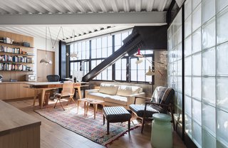 Old concrete walls, multi-pane windows, and glass block walls hint at the previous life of this loft building as a garage. The glass block partition divides the living room from the bathroom and acts as a stylish buffer between the two spaces.