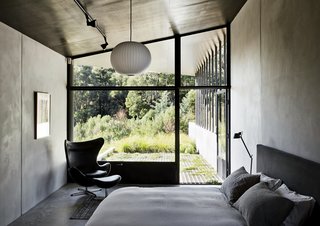 The master bedroom, which features a bed by Paolo Piva, an Egg chair by Arne Jacobsen, and a Ball pendant lamp by George Nelson, opens directly onto a verdant patio. The metal shutters at the bottom of the window keep out flying embers in case of fire.