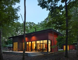 Nestled in a forest, the residence consists of three volumes. The patio, enhanced by a German-made beer garden table, is an extension of the living room floor, creating an indoor-outdoor living space. "It’s one way a small space can be made to feel larger," says architect Jason W. Hart. All of the exterior doors are painted marigold, providing a friendly pop of color.