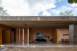 The home’s living room can be kept open to the elements, or sectioned off with sliding glass walls. A natural concrete slab acts as an exterior barrier, and freijó wood and track lighting define the interior space. C10 sofa by Marcus Ferreira and vintage Poltrona Molé chair by Sergio Rodrigues provide casual seating. Across the partition wall, a Jader Almeida table anchors the dining room.