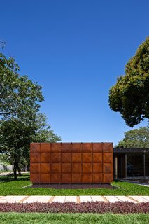 The geometric front facade of the home is made of Cor-Ten steel, segregated into eight vertical panels. Juxtaposed with its lush natural environment, the front elevation is a minimal and abstract counterpoint to its surroundings. An exterior pool meets the facade at its base.