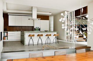 A Tranquil Lakeside Abode in Quebec Unfolds Over Six Levels - Photo 9 of 9 - "Riftcut oak panels are used in woodworking and on some kitchen walls," said Tremblay. The design of the cabinets is by Tremblay’s firm, Boom Town, with fabrication by Atelier Boisteck. Stools by Arteriors are lined in front of a granite countertop from Costa Esmeralda.