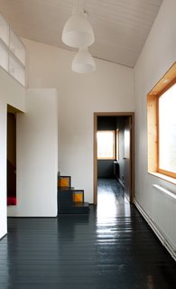 A pair of lights from IKEA hang above the first floor, which houses the living room, kitchen, and bathroom. Pine floors, painted black, run throughout the residence.