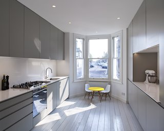 The owners, a couple with small children, sought to bring openness into the cramped space, and create a bright and functional home for their family. London-based practice Russian For Fish worked intimately with the owners to bring their vision to life, all while adhering to a strict project budget of under $150,000. Throughout the home, the original strip-wood floorboards were preserved and painted a soft, muted gray. The cool tones of the kitchen are punctuated by a bright yellow children's table that sits near the bay window.
