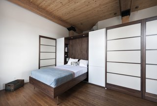 In an 850-square-foot loft in Montreal, Quebec–based firm Gepetto built understated, custom cabinetry to suit an aging couple's needs. Here, the Murphy bed that folds into a larger walnut storage unit. The wall, which also conceals a washer and dryer, does double duty as a partition between the bedroom and the loft’s entrance. Modern Murphy beds like this one often incorporate sleek lines constructed in dark-toned woods. 