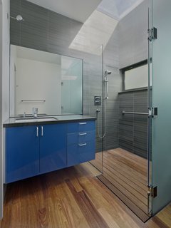 An Indoor-Outdoor Renovation for a 1950s Ranch House in the Bay Area - Photo 6 of 8 - A custom skylight floods the bathroom with light. A tempered glass shower and Grohe faucet accent the space; custom glossy cabinetry with Hafele hardware again adds a pop of color.