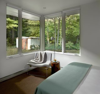 The modest bedroom looks towards the yard and part of the owner’s garden. The table, by Jayson Home, holds a vintage lamp and is flanked by a Spring Lounge chair by Cappellini.