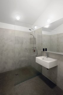 Milestones' cement plaster covers the walls of the minimalist bathroom. The Scola sink from Duravit is accompanied by a chrome Grohe Essence faucet and Hansgrohe's Croma Green Showerpipe.