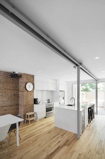 In the kitchen, glossy white MDF and quartz countertops allow for maximum light reflection, as do the white walls and ceilings. The stools are from Zone Maison.