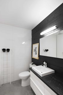 The walls of the bathroom are covered in large, white ceramic tiles, with the exception of one side clad in reclaimed wood with an IKEA cabinet.